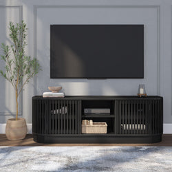 Modern living room with a wall-mounted flat-screen TV above a black slatted media console, woven basket and decorative books on the console, potted olive tree and candle on a gray paneled wall, hardwood floor and neutral area rug, minimalist home decor.