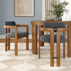 Modern dining room interior with round wooden table and matching wood chairs upholstered in blue‑gray fabric, neutral abstract wall art, green glass vase with leafy plant, cream curtains and textured beige rug