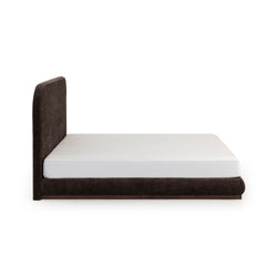 Side view of modern low-profile brown upholstered platform bed with tall rounded headboard and white mattress on white background