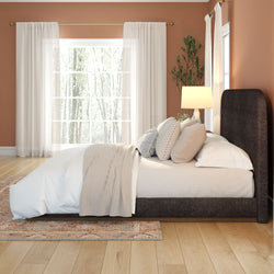 Cozy modern bedroom with dark upholstered platform bed, neutral linen bedding, patterned pillows, sheer curtains and hardwood floors