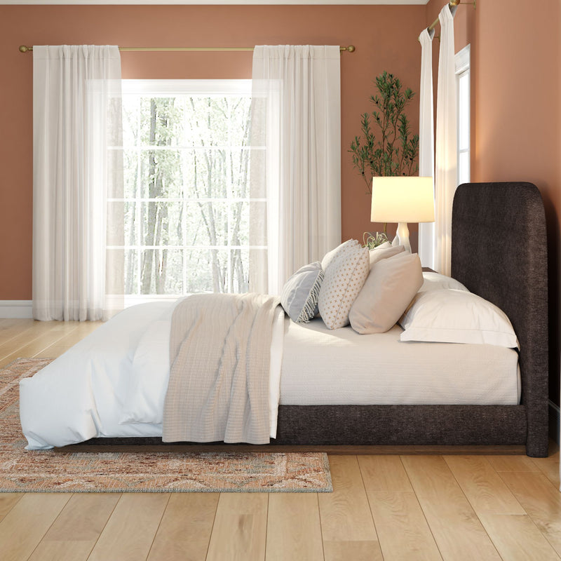 Cozy modern bedroom with dark upholstered platform bed, neutral linen bedding, patterned pillows, sheer curtains and hardwood floors