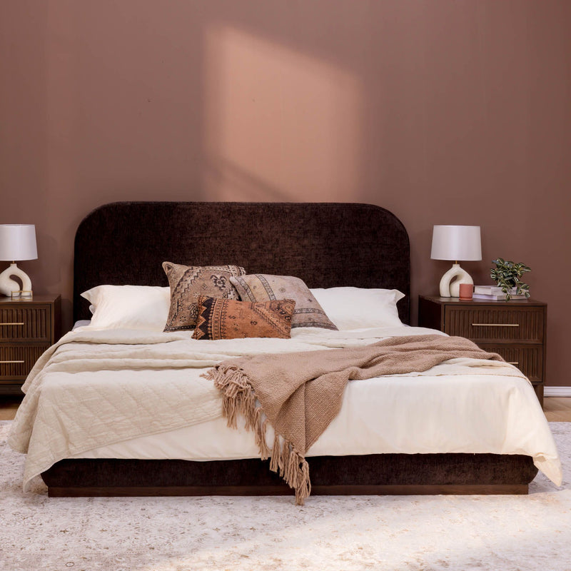 Modern bedroom with dark headboard, beige bedding, and vintage pillows.