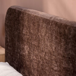 Plush brown fabric headboard of a bed against a soft pink wall.