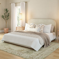 Elegant bedroom interior with well-lit natural light, featuring a cozy bed, beige throw pillows, and neutral decor.