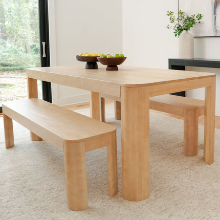 Modern wooden dining table with benches in a bright dining room, featuring fruit bowls and minimalist decor.