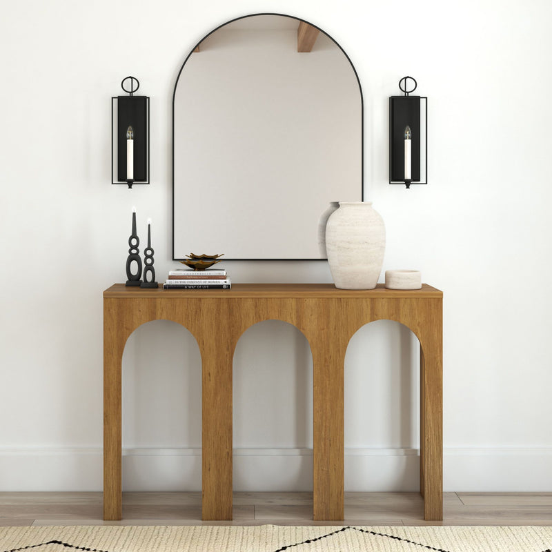 Modern wooden console table with decorative vases and books in entryway with arched wall mirror.