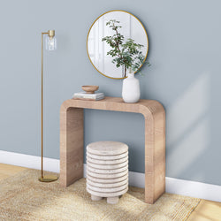 Minimalist entryway with light-wood curved console table against a powder blue wall, round gold-framed mirror, white ceramic vase with greenery, gold floor lamp and textured natural rug