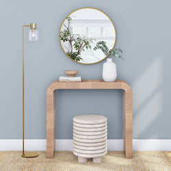 Modern living room interior with decorative console table, round mirror, contemporary floor lamp, and unique stone stool on beige rug.