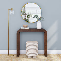Modern interior design with wooden console table, ceramic stool, round mirror, and decorative floor lamp against a light blue wall.