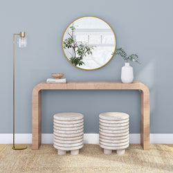 Modern minimalist entryway against a soft blue wall with a light wood console table, round gold-framed mirror, stacked ceramic stools, white vase, and brass floor lamp