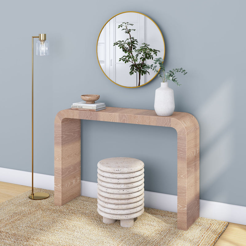 Modern entryway wood console table with round gold mirror, white vase with eucalyptus, stacked stone stool, gold floor lamp and neutral rug on blue-gray wall