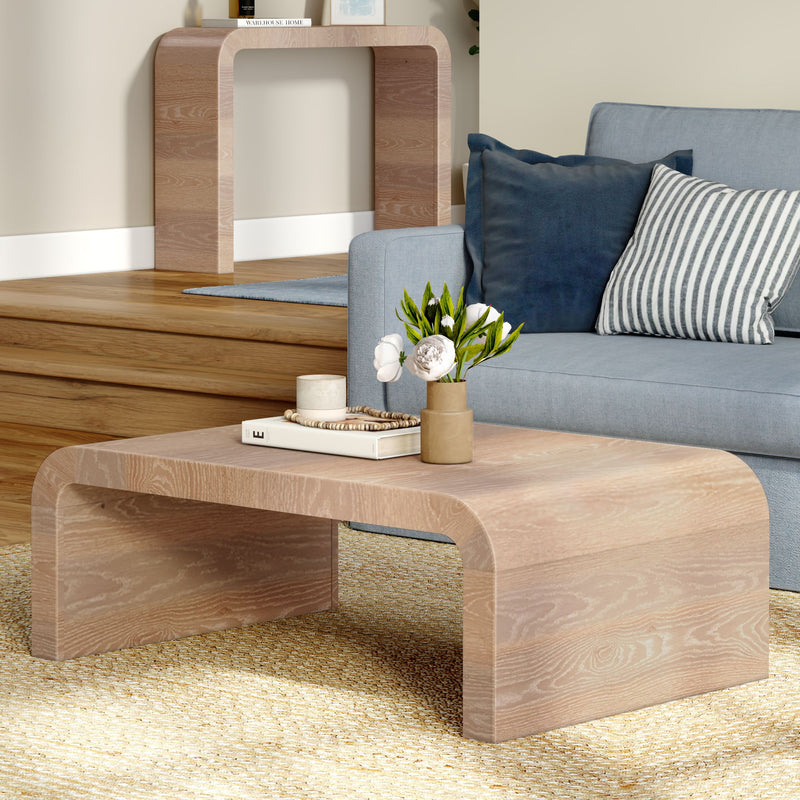 Light oak curved modern coffee table in a Scandinavian living room with a blue sofa, striped and navy cushions, vase of white flowers, book and candle on a woven rug