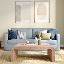 Cozy modern living room with light blue sofa, striped throw pillows, curved wooden coffee table and neutral wall art