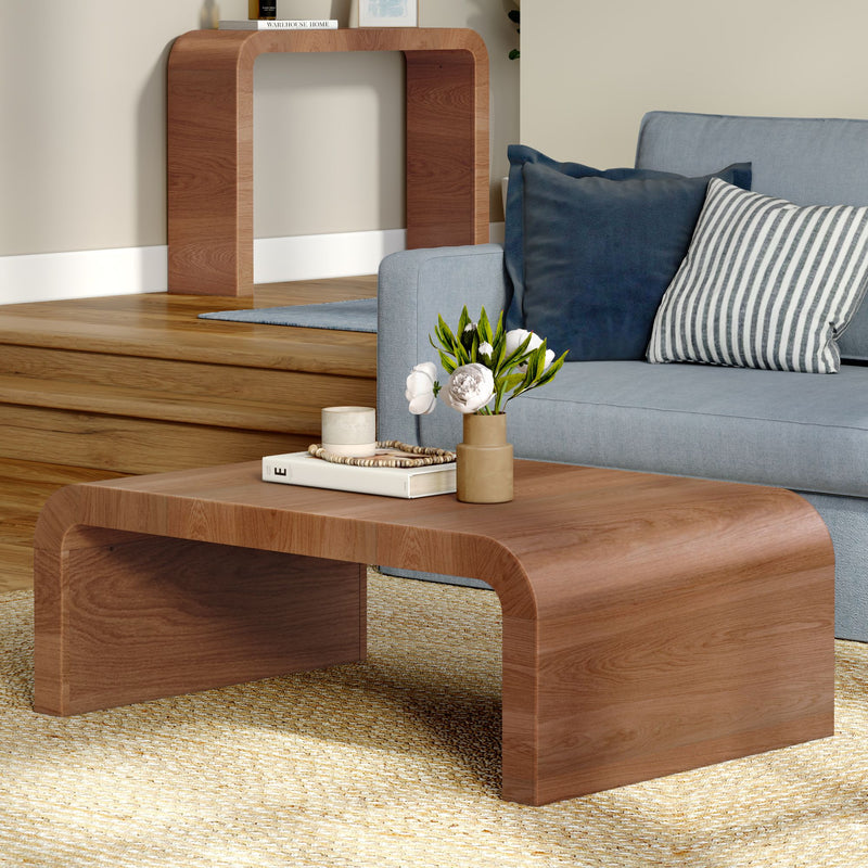 Curved wooden coffee table in living room with blue sofa, striped pillow and vase of white flowers on hardwood floor