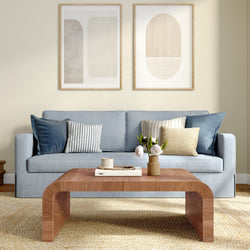 Scandinavian modern living room interior with light blue sofa, striped and textured accent pillows, curved wooden coffee table with vase of white flowers, abstract framed wall art and neutral beige rug, minimalist home decor