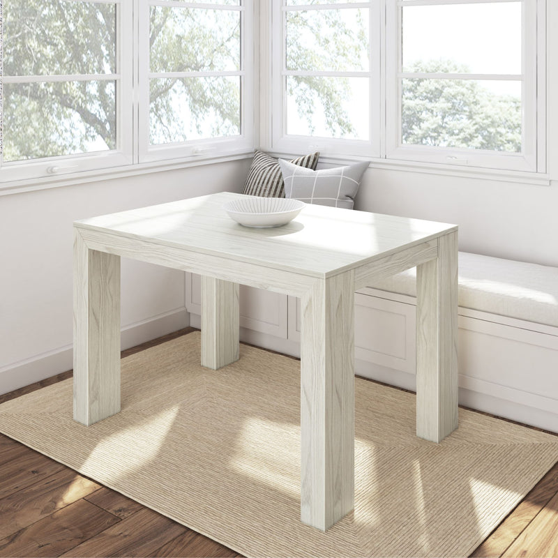 White wooden dining table in a bright sunlit room with cushioned window seating.