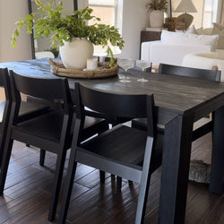 Modern dining room with a black wood table, black chairs, and a centerpiece of green leaves in a white vase.