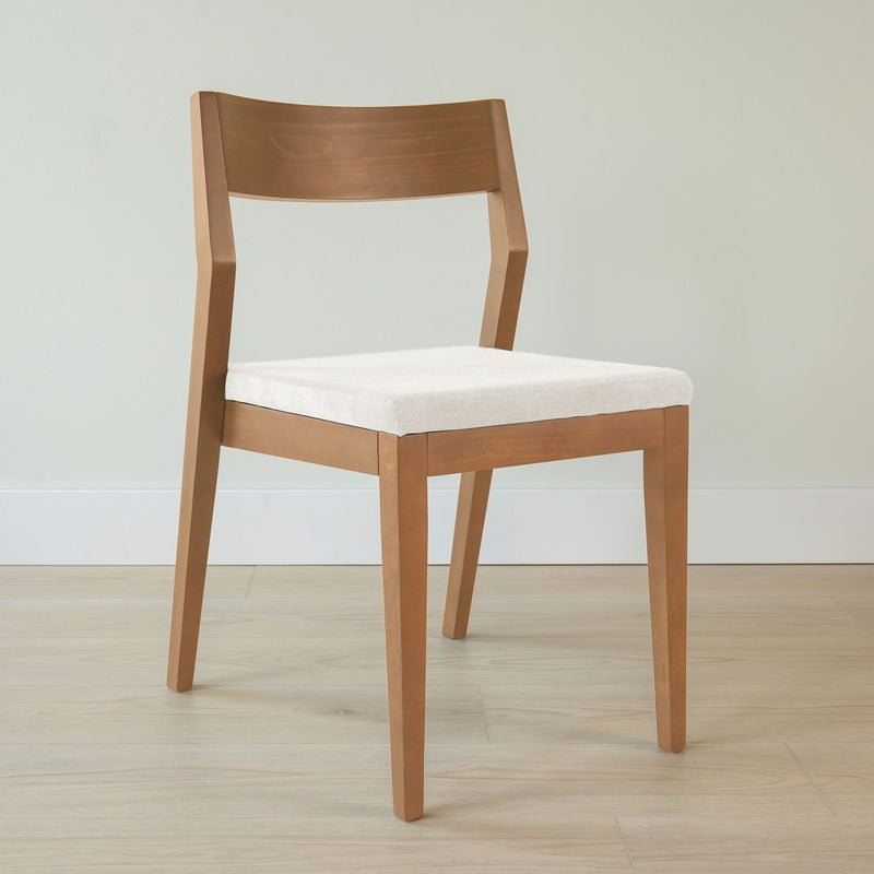 Wooden dining chair with a white cushion on a light-colored floor against a neutral wall.