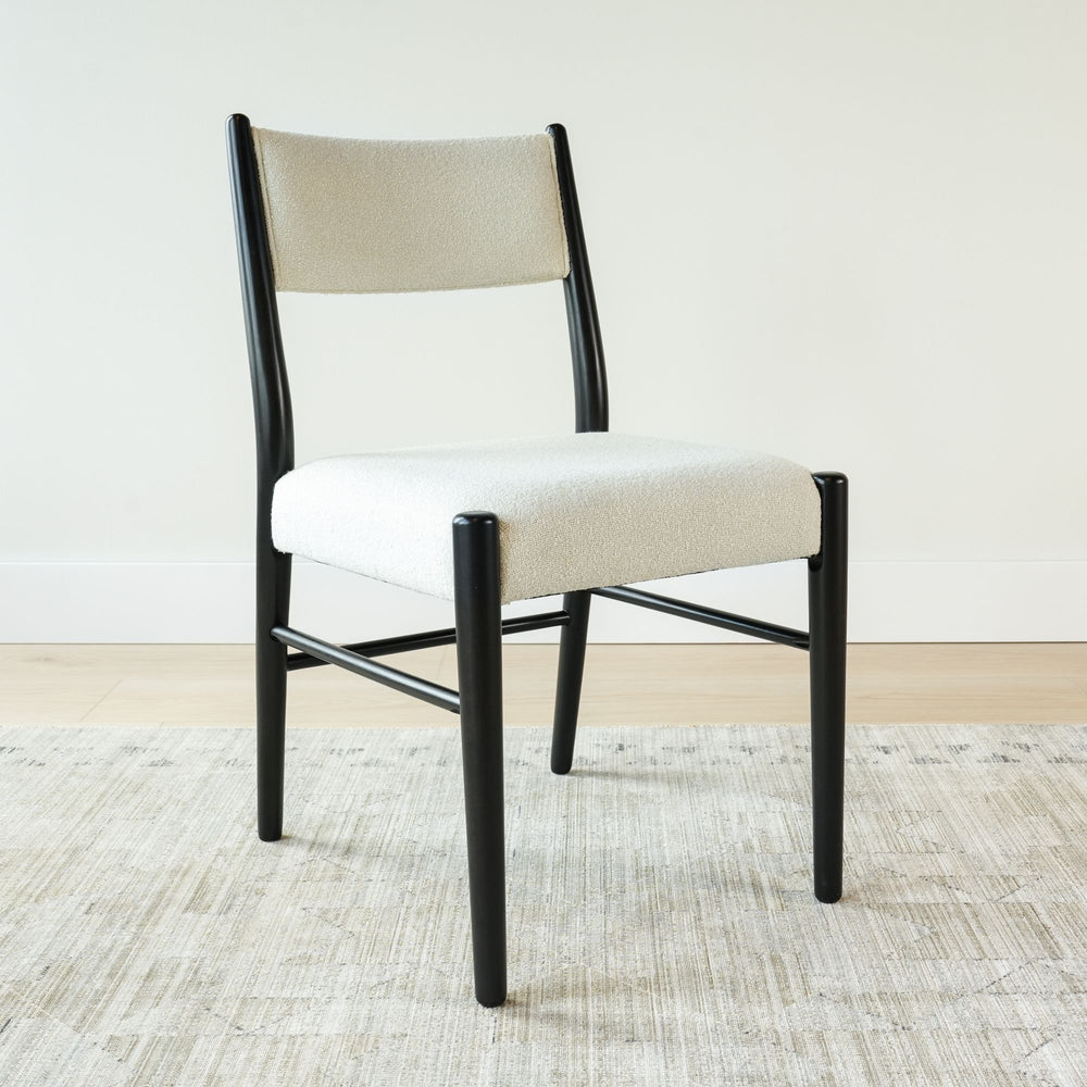 Mid-century modern chair with black frame and cream upholstery on a light hardwood floor.