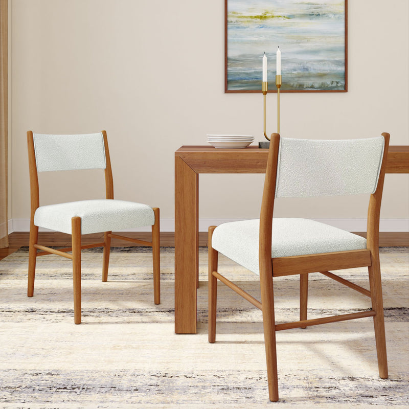 Two mid-century modern wooden dining chairs with white upholstered seats beside a wood dining table in a neutral dining room with abstract wall art, brass candlestick and patterned area rug