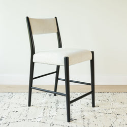Modern black-framed dining chair with cream boucle upholstered seat and back on textured area rug and light wood floor