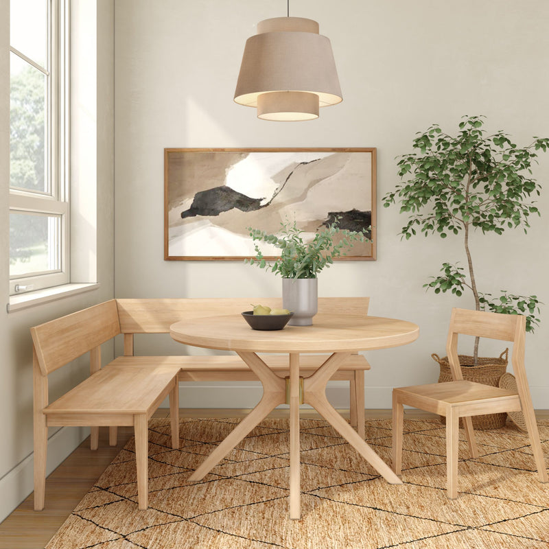 Light wood round dining table in a Scandinavian breakfast nook with corner bench seating, beige pendant light, abstract wall art, woven rug and potted plant