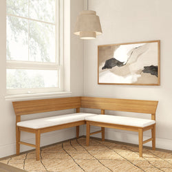 Light oak corner bench with white cushions in bright dining nook, neutral abstract wall art, pendant lamp and woven jute rug