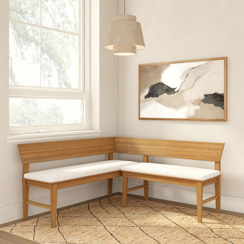 Light oak corner bench with white cushions in bright dining nook, neutral abstract wall art, pendant lamp and woven jute rug
