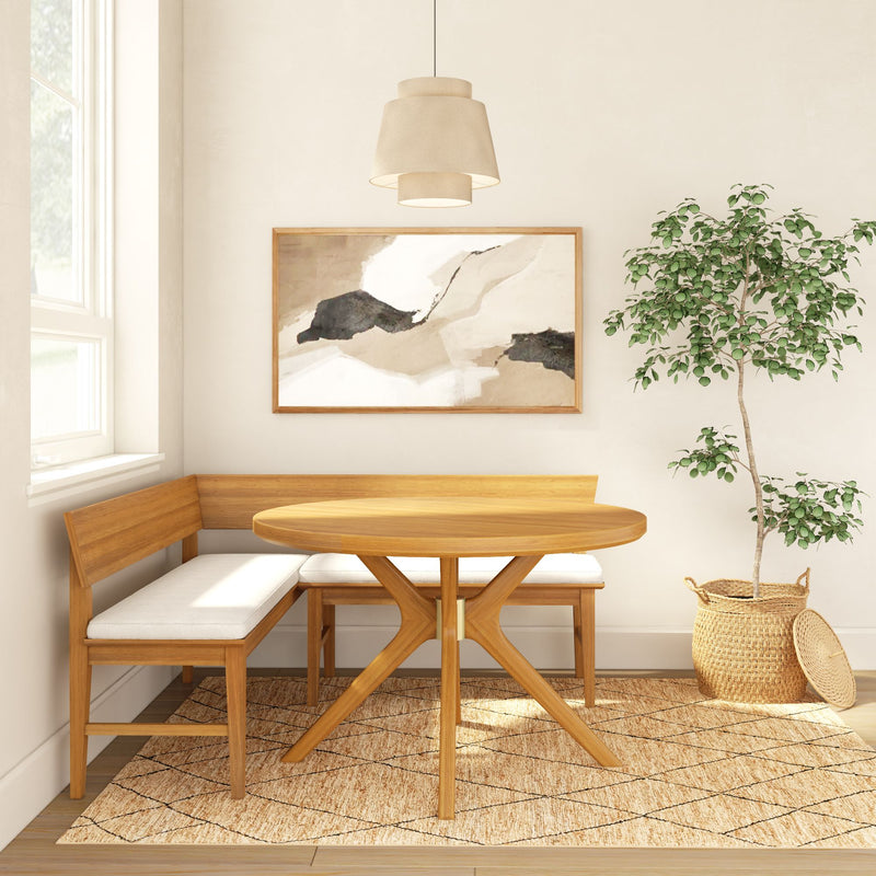 Sunlit Scandinavian-style dining nook with round wooden table, corner bench seating with white cushions, abstract framed art, pendant lamp, woven jute rug and potted ficus in a wicker basket