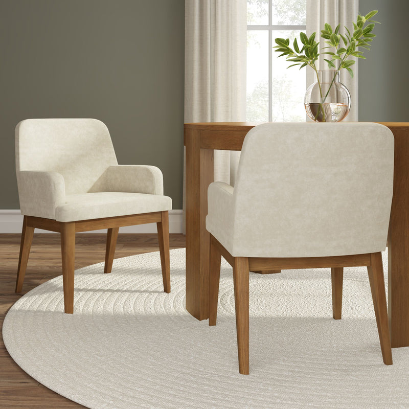 Pair of mid-century modern beige upholstered dining chairs with solid wood legs beside a wood dining table on a round cream rug, vase with green foliage and neutral wall