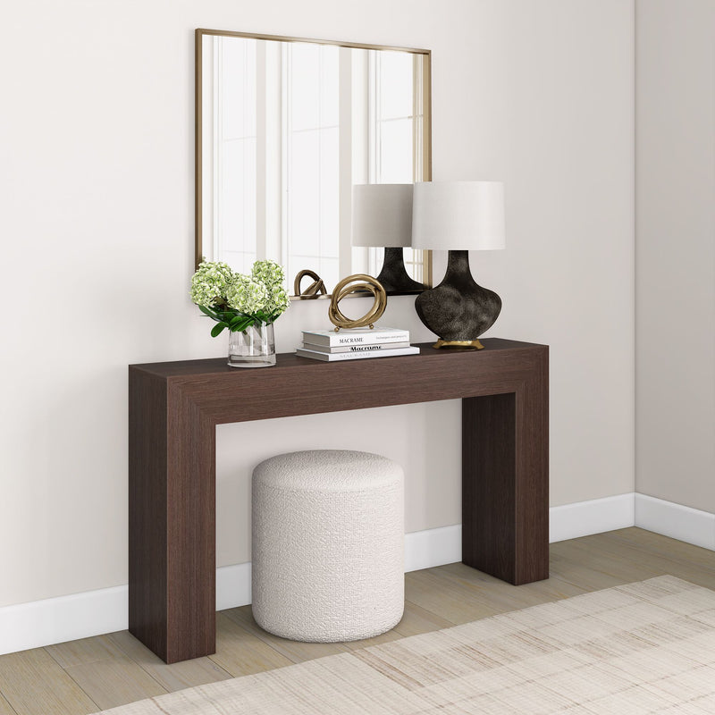 Modern entryway with a dark wood console table, white round ottoman, decorative mirror, table lamps, and green plant arrangement.