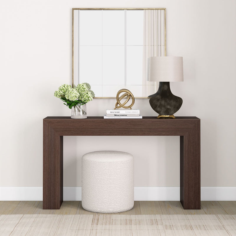 Modern minimalist entryway with a dark wood console table, decorative mirror, elegant table lamp, and white ottoman featuring home decor accents.