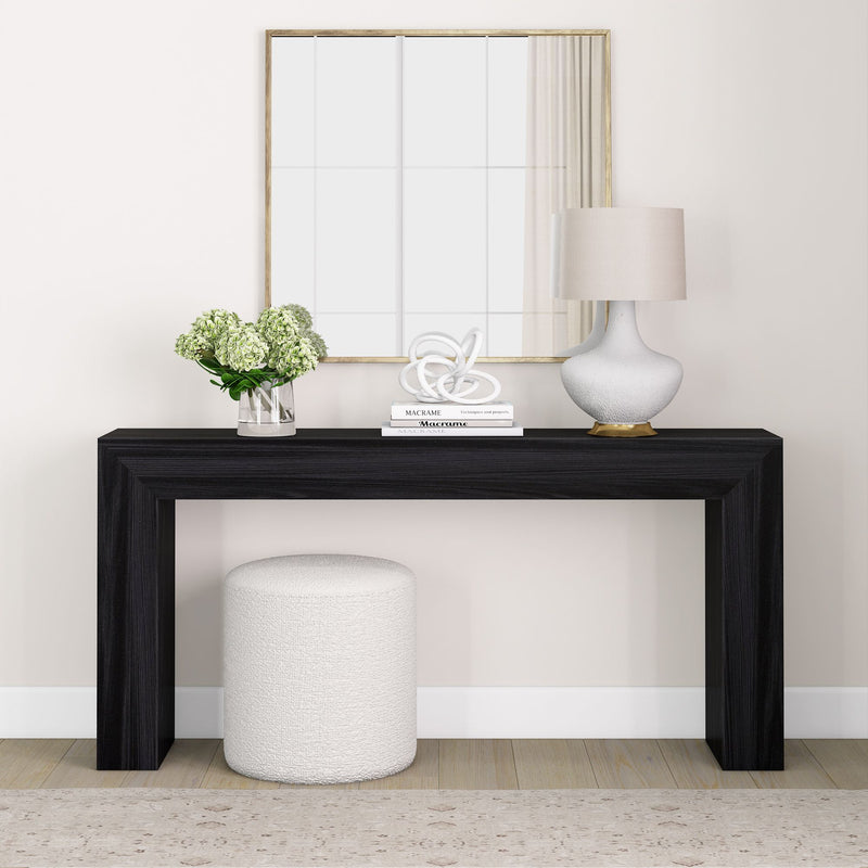 Minimalist living room with black console table, white ottoman, and decorative elements including a glass vase and lamp.