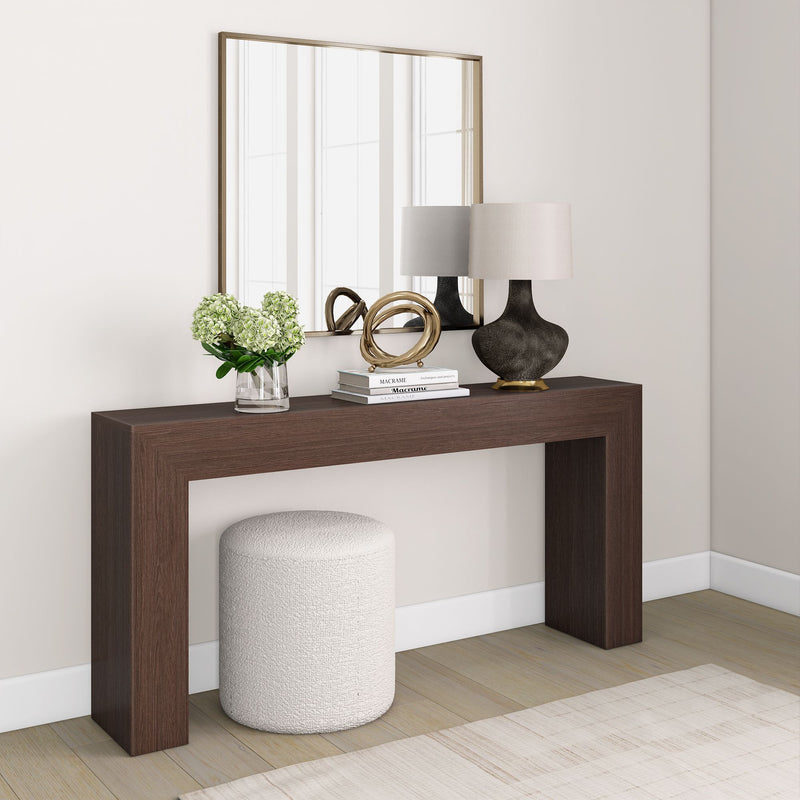 Modern hallway interior with dark wood console table, decorative mirror, round ottoman, contemporary lamp, and floral arrangement.