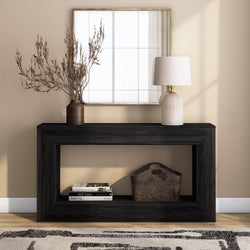 Minimalist modern entryway console table in black wood styled with a gold-framed mirror, ribbed ceramic table lamp, brown vase of dried branches, storage basket and stacked coffee-table books against a beige wall