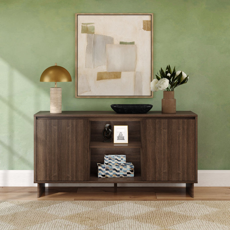 Modern dark wood console table on a green accent wall with abstract framed art, gold table lamp, black decorative bowl, brown vase of white flowers, patterned storage boxes, hardwood floor and textured rug — stylish entryway decor