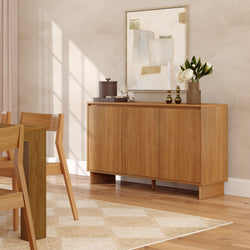 Mid-century modern wooden sideboard in a bright dining room with natural wood table and chairs, abstract framed art, brass candlesticks, white peony vase and hardwood floors.