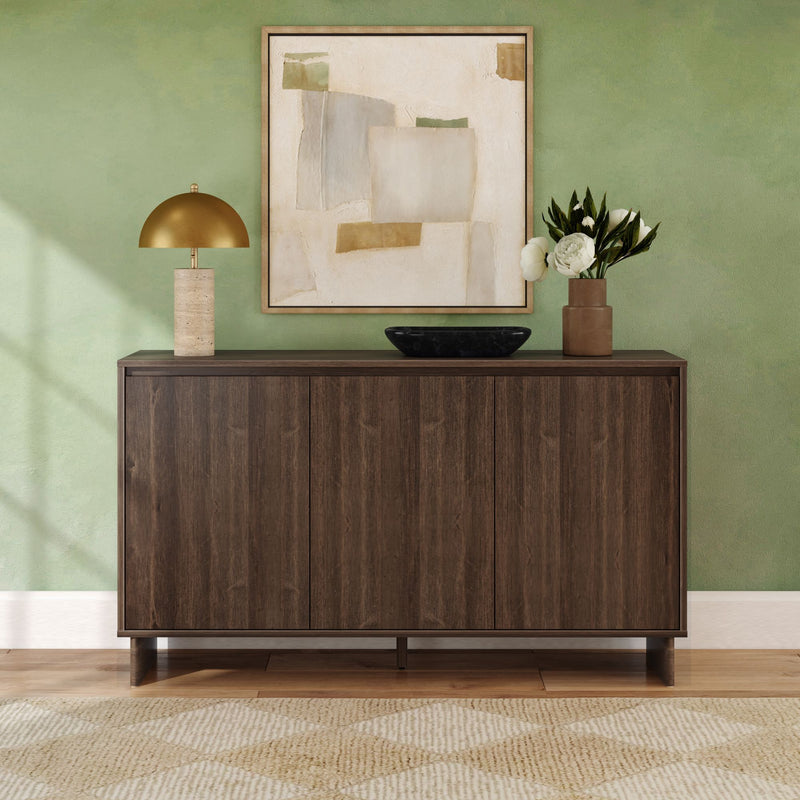 Dark wood sideboard console in a modern entryway against a green accent wall with framed abstract art, gold dome table lamp, brown vase of white peonies and black decorative bowl on a hardwood floor with patterned rug