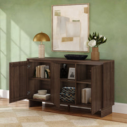 Dark walnut modern sideboard/console cabinet with open doors revealing shelves of books and decor, topped with a gold dome lamp, black bowl and vase of white flowers beneath abstract wall art in a green-walled living room