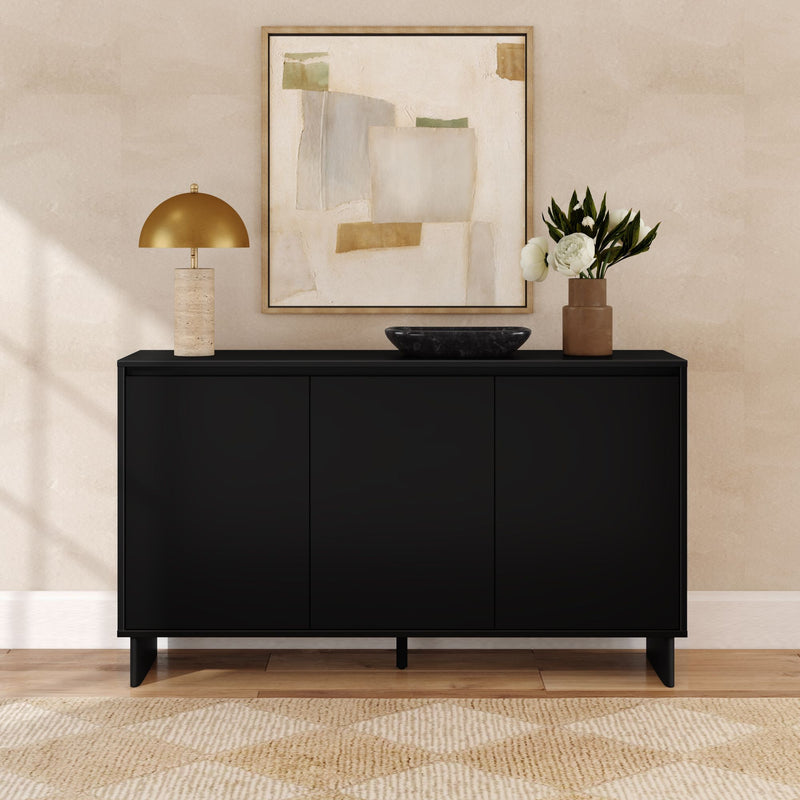 Modern black sideboard console in a minimalist entryway with gold table lamp, abstract wall art, black bowl and vase of white flowers on wood floor