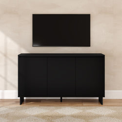 Black media console cabinet with three doors under wall-mounted flat-screen TV in a minimalist beige living room on hardwood floors