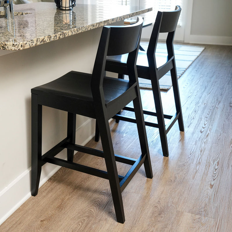 Black wooden bar stools under granite kitchen counter in modern home interior.