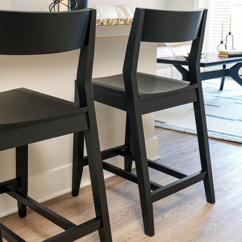 Black wooden bar stools at modern kitchen island with light flooring in bright interior setting.