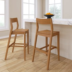 Modern bar stools with wooden design in a bright kitchen setting, featuring a white marble countertop and a bowl of oranges for decoration.