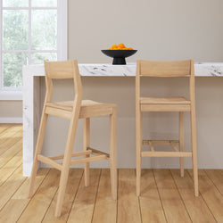 Two wooden bar stools at a marble kitchen counter with a fruit bowl filled with oranges.