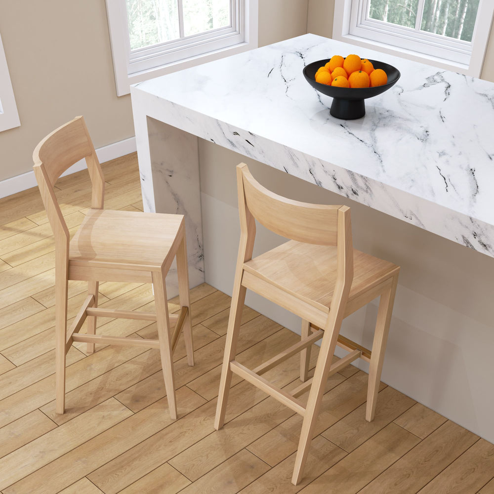 Two wooden bar stools next to a modern marble kitchen countertop with a black bowl of oranges, showcasing home interior design.