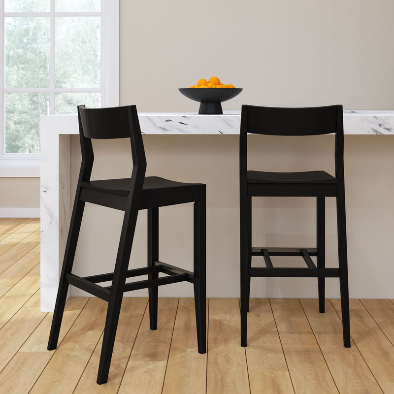 Modern black bar stools at a white marble kitchen counter with a bowl of oranges in a bright, minimalist kitchen setting.