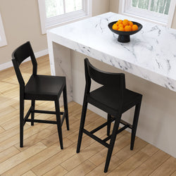 Black modern bar stools at a white marble kitchen island with a bowl of oranges.
