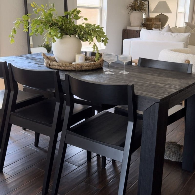 Modern dining room with black wood table and chairs, featuring a decorative plant centerpiece and elegant decor accents.