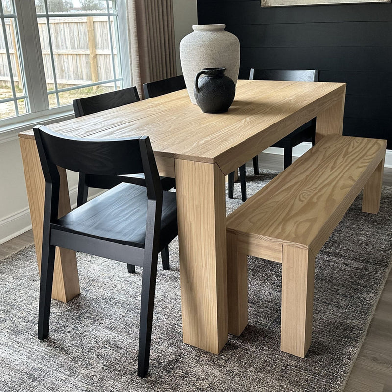 Modern minimalist dining room setup with a wooden table, black chairs, and a matching bench, accented by decorative vases.